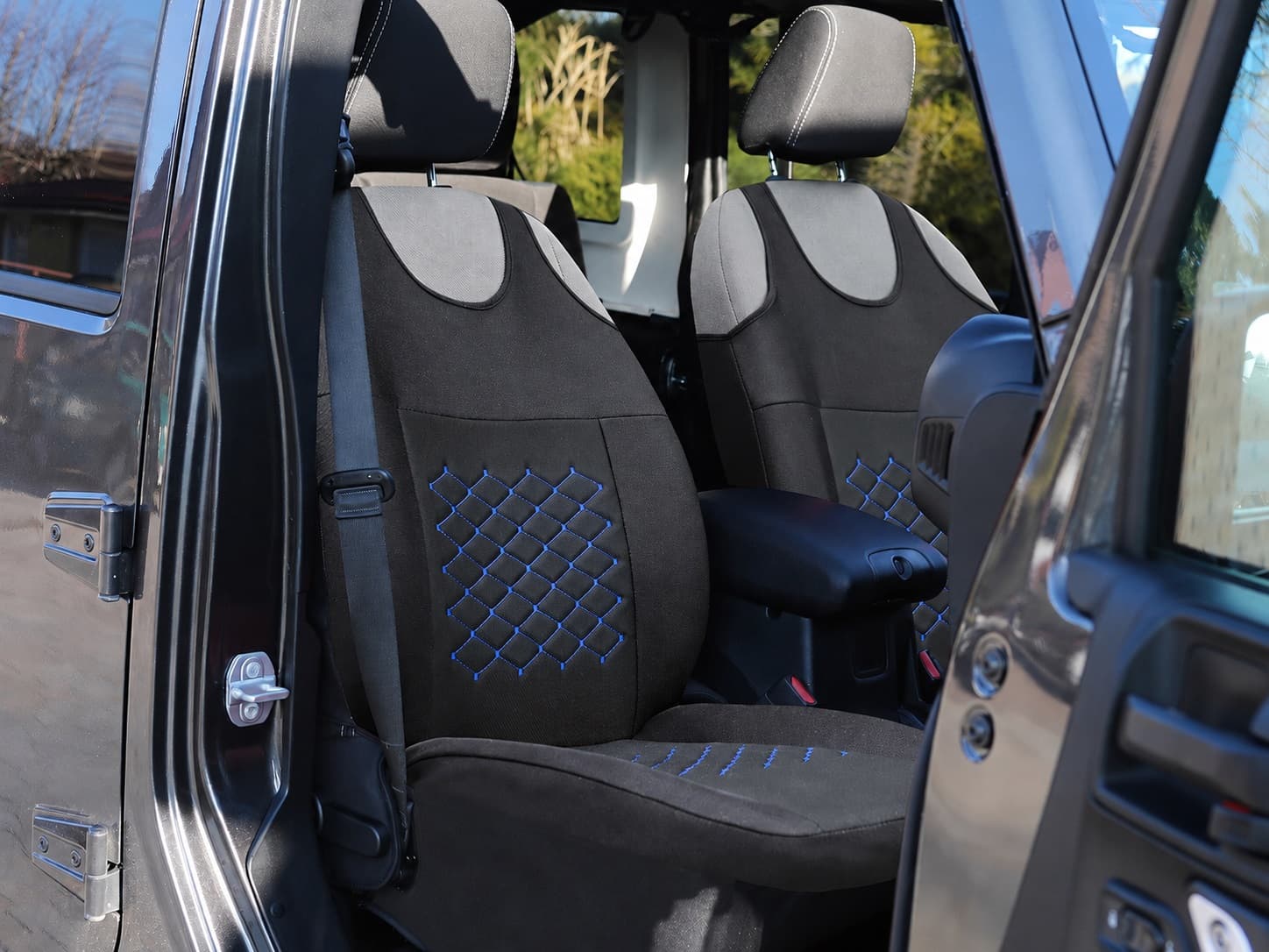 Fundas de asiento tipo camiseta Motive negras con costuras azules montadas en los asientos delanteros de un coche